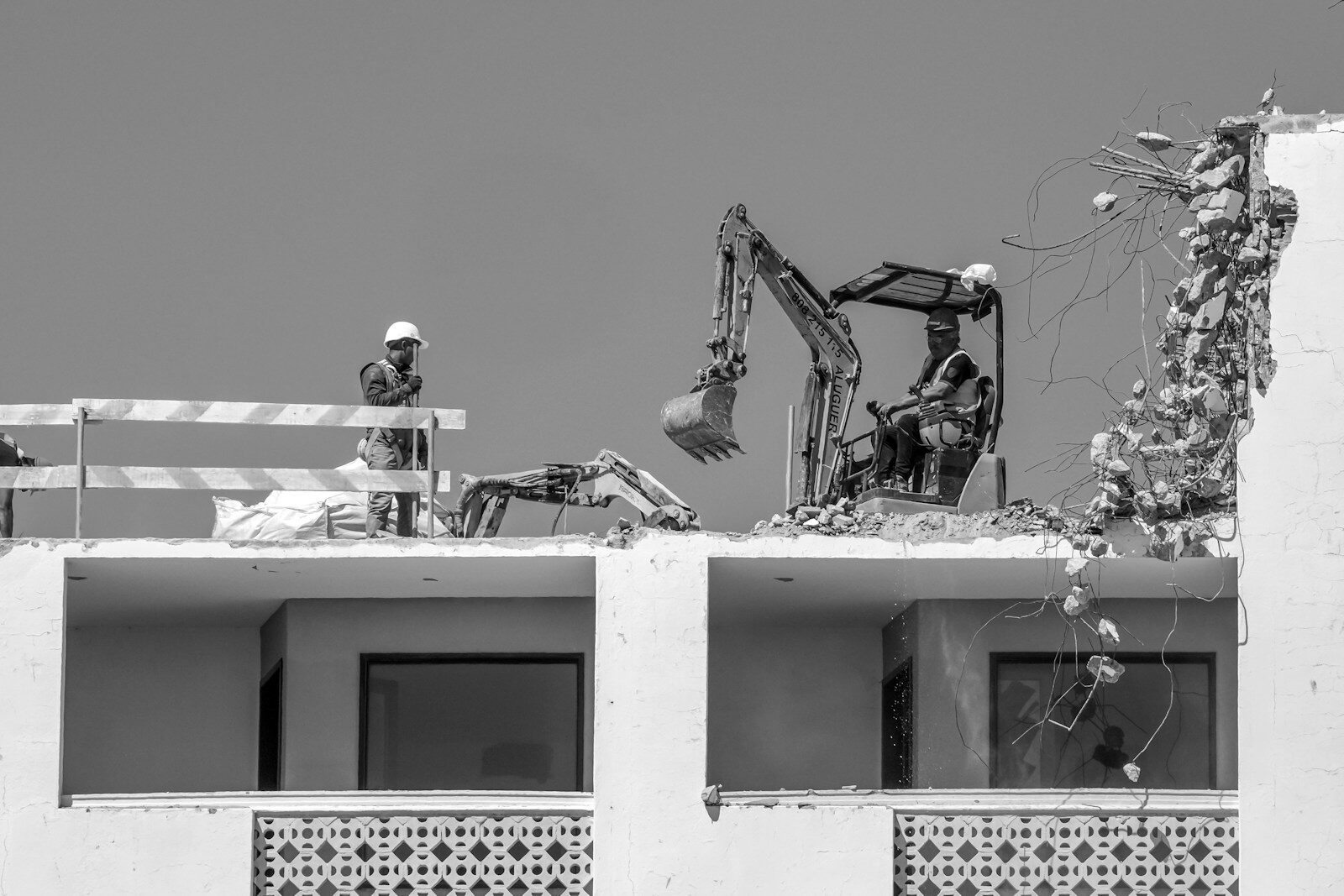 Workers demolish a building with an excavator and tools.
